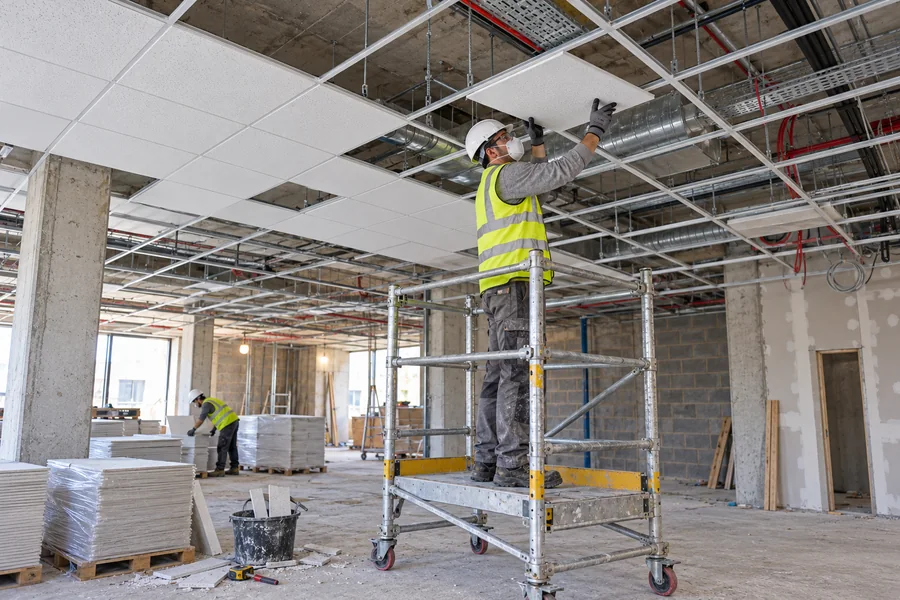 Worker installing a suspended ceiling tile from a mobile scaffold